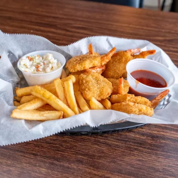 Fried shrimp and french fries in a basket with coleslaw and cocktail sauce.