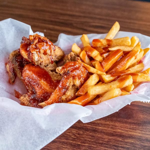 BBQ chicken wings and french fries drizzled with sauce, served in a white paper-lined basket.